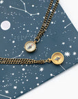 Two vintage compass necklaces on brass chains on a celestial themed background