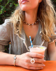 Woman holding a pink drink with a straw at an outdoor setting with a vintage hand-painted bracelet