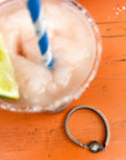 Close-up of a drink with a lime wedge and a straw, with a vintage hand-painted bracelet on an orange surface.