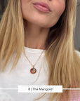 A close-up of a woman wearing a delicate gold chain necklace with a round red and gold micro mosaic pendant, paired with a white t-shirt.