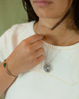 A close-up lifestyle shot of a person wearing a silver pendant necklace with a small colorful circular micro mosaic charm and a matching gold bracelet.