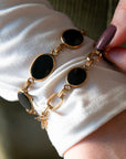 Detailed close-up of two vintage gold-filled bracelets with black onyx cabochons worn on a wrist.