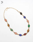 A gold-tone chain necklace featuring multiple oval cabochon gemstone beads in various colors including pink, green, blue, brown, and red, arranged in a circular layout on a white background.