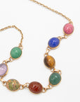 Close-up of a scarab gemstone necklace highlighting the carved beetle details in pink, blue, tiger's eye, and green stones.