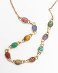 Two scarab gemstone necklaces crossing each other, displaying their carved multicolor stone beetles in pink, blue, green, and red tones.