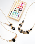 Three gold-fill onyx necklaces including winged, nine-stone, and drop designs displayed with a holiday ornament resembling a watercolor paint palette