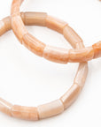 Close-up of two peach-toned sunstone beaded bracelets overlapping against a white background, highlighting their tumbled cylindrical beads.