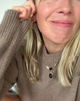 A close-up lifestyle shot of a woman wearing a gold necklace with a black teardrop onyx pendant and a gold hoop earring.