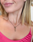 A close-up of a woman wearing a delicate antique bronze chain necklace with a small oval-shaped pendant and a dog clip at the bottom, paired with a bright pink top.