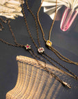 Three antique Victorian-era lariat chatelaine slider necklaces with decorative pendants arranged on a dark textured surface with a woven basket and dried flowers as props. The necklaces feature a star pendant with a red gem, a floral pendant with a red gem and clear stones, and a small gold heart pendant.