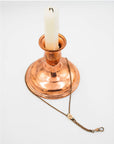 Copper candle holder with a white candle on a light gray background holding an antique grand deco chatelaine slider necklace