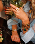Woman's wrists stacked with multiple vintage gold-filled bracelets with varying colorful stones holding a cocktail glass.