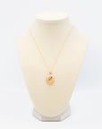 Vintage oval gold locket with unique engraving displayed on a white jewelry bust