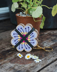 Studio Wald Periwinkle flower press keychain on a garden table with daisies
