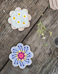 Two Studio Wald flower press keychains on weathered wood, one open with pressed daisies