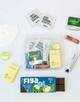TME Flight Kit contents: lip balm, hand cream, mints, sanitizer spray, cupuaçu chocolate bar, pill case, K95 mask, and essential oil towelettes.