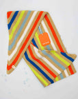 Folded Verloop triangle scarf in bright stripes with its orange hang tag