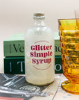 Wood Stove Kitchen Glitter Simple Syrup bottle beside an amber glass and books
