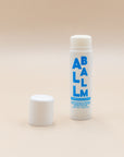 Uncapped Zizia All Balm stick beside its cap on a beige background