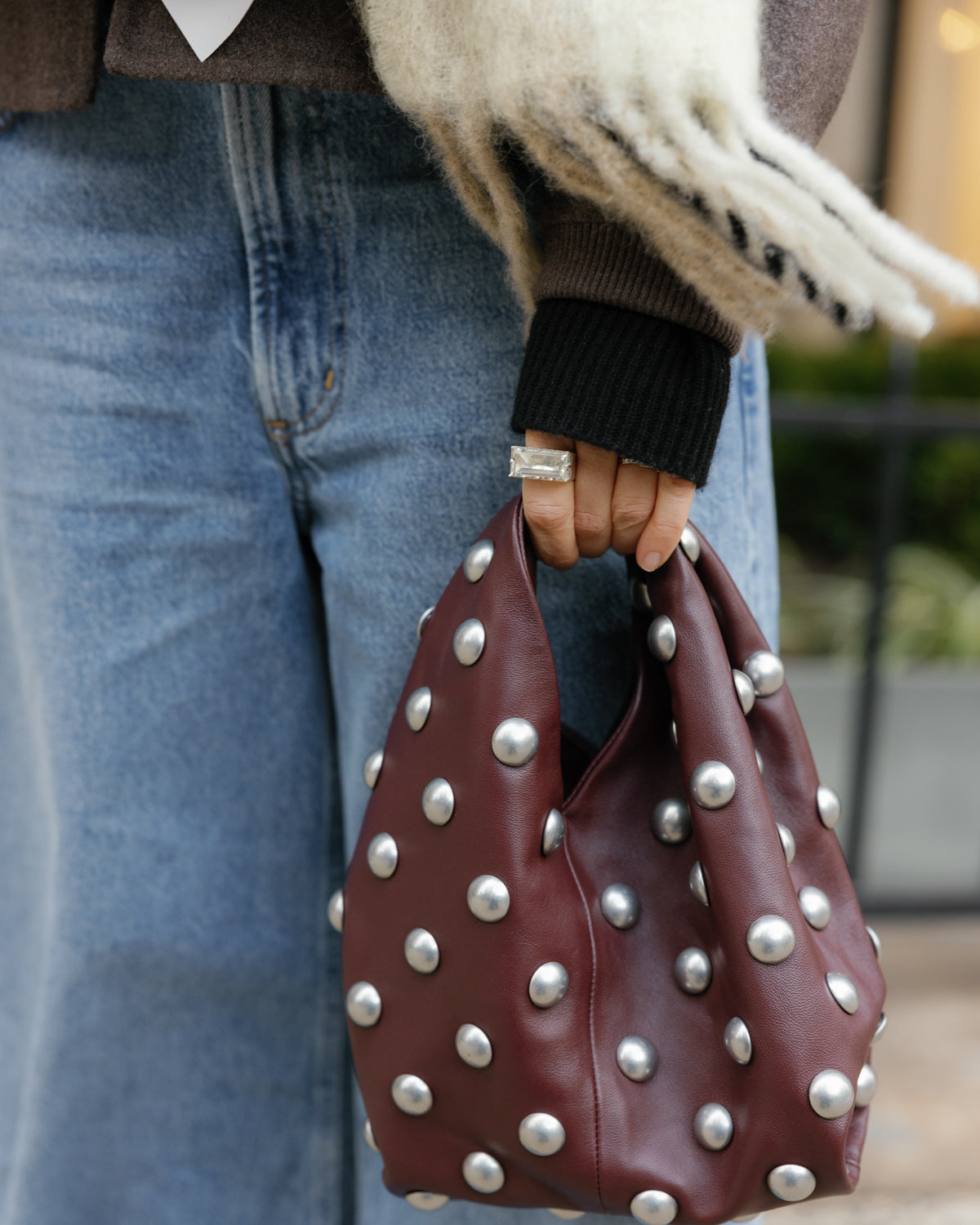 Leather handbag with silver studs held by a person wearing a silver and clear quartz ring.