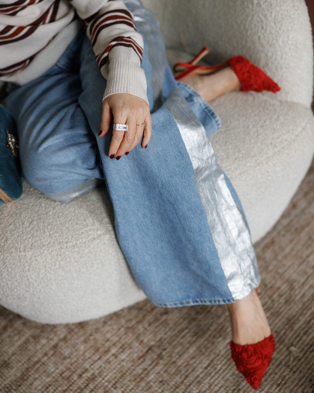 Person wearing a striped sweater and blue jeans with The East/West silver and clear quartz ring sitting on a couch with red shoes.