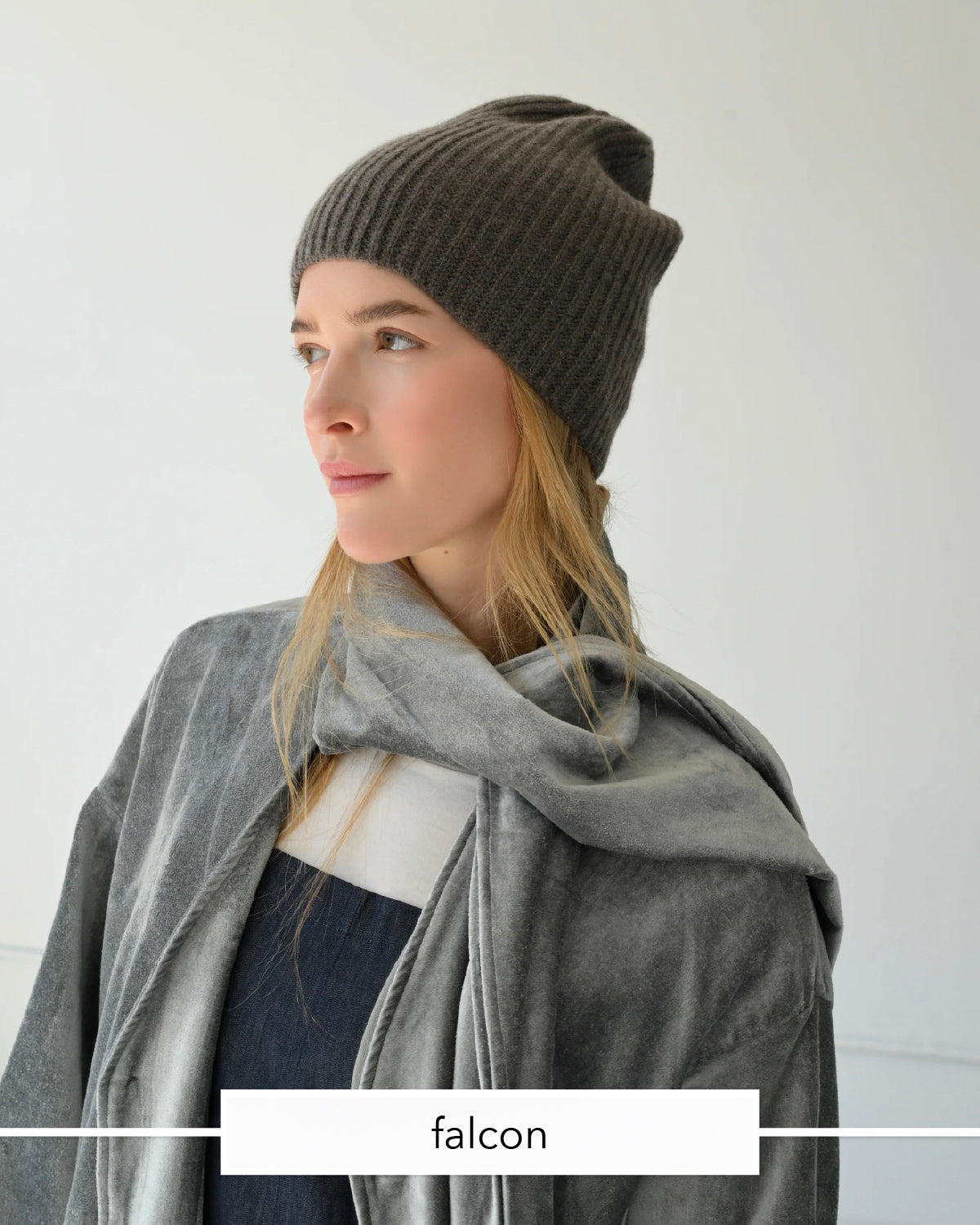 A woman wearing a dark brown ribbed knit beanie, a gray scarf, and a navy top, shown in profile against a light gray background. A white label at the bottom reads 'falcon'.