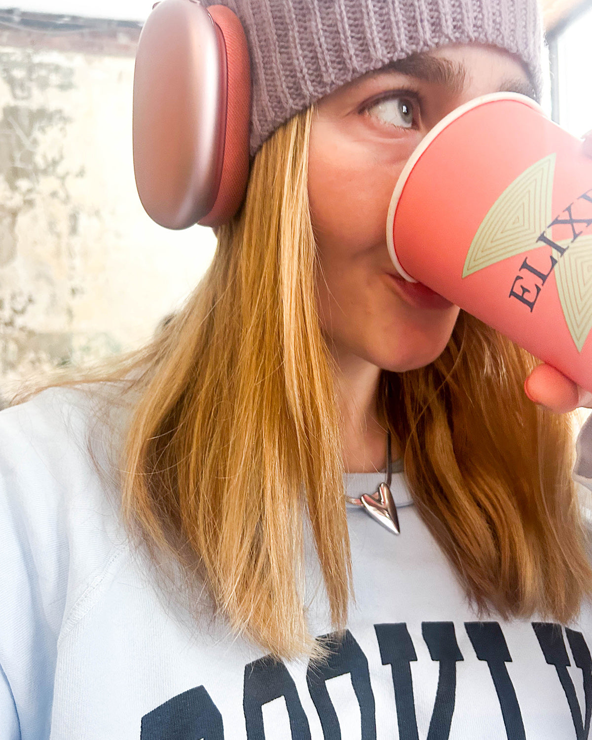 Person wearing a light purple 8.6.4 cashmere knit beanie and headphones, holding a pink mug