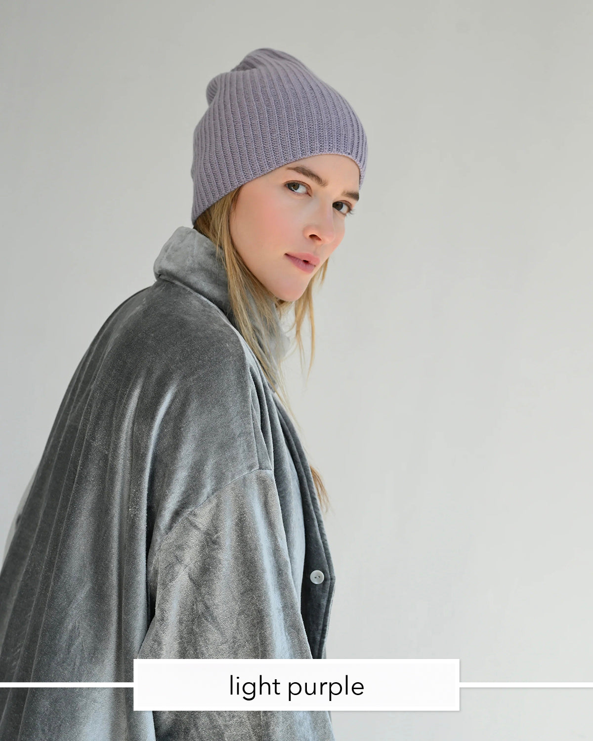 A woman wearing a light purple ribbed knit beanie and a gray plush jacket, shown in profile against a plain light gray background. A label at the bottom reads 'light purple'.