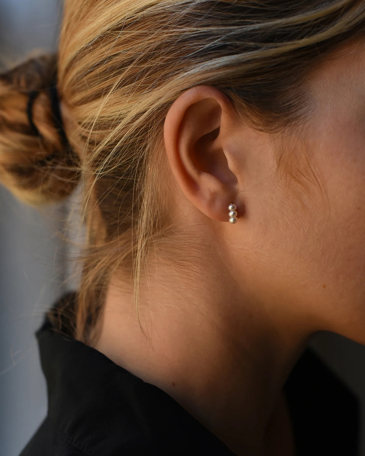 Close up of woman wearing a modern pair or 8.6.4  pearl earrings, featuring a trio of freshwater pearls.