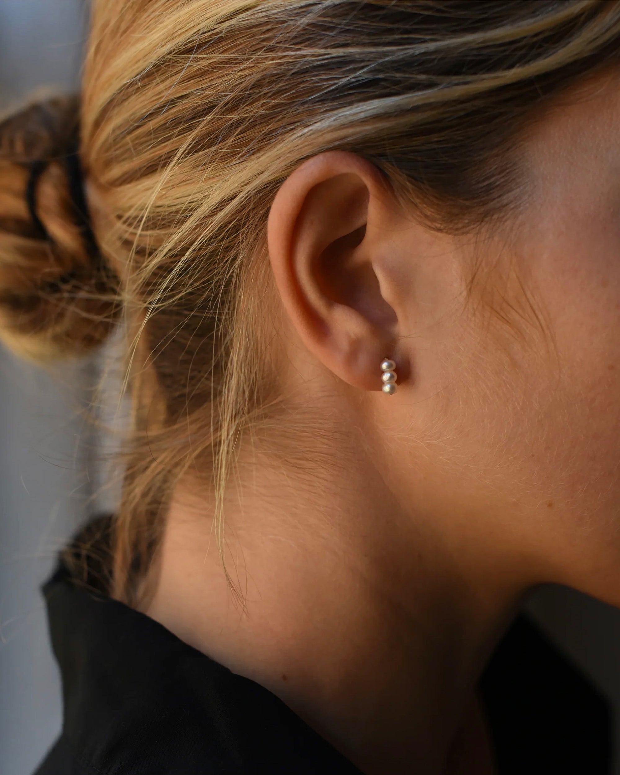 Close up of woman wearing a modern pair or 8.6.4  pearl earrings, featuring a trio of freshwater pearls.