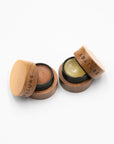 Two open Abature lip pots with wood lids: strawberry lip scrub and plumping lip serum