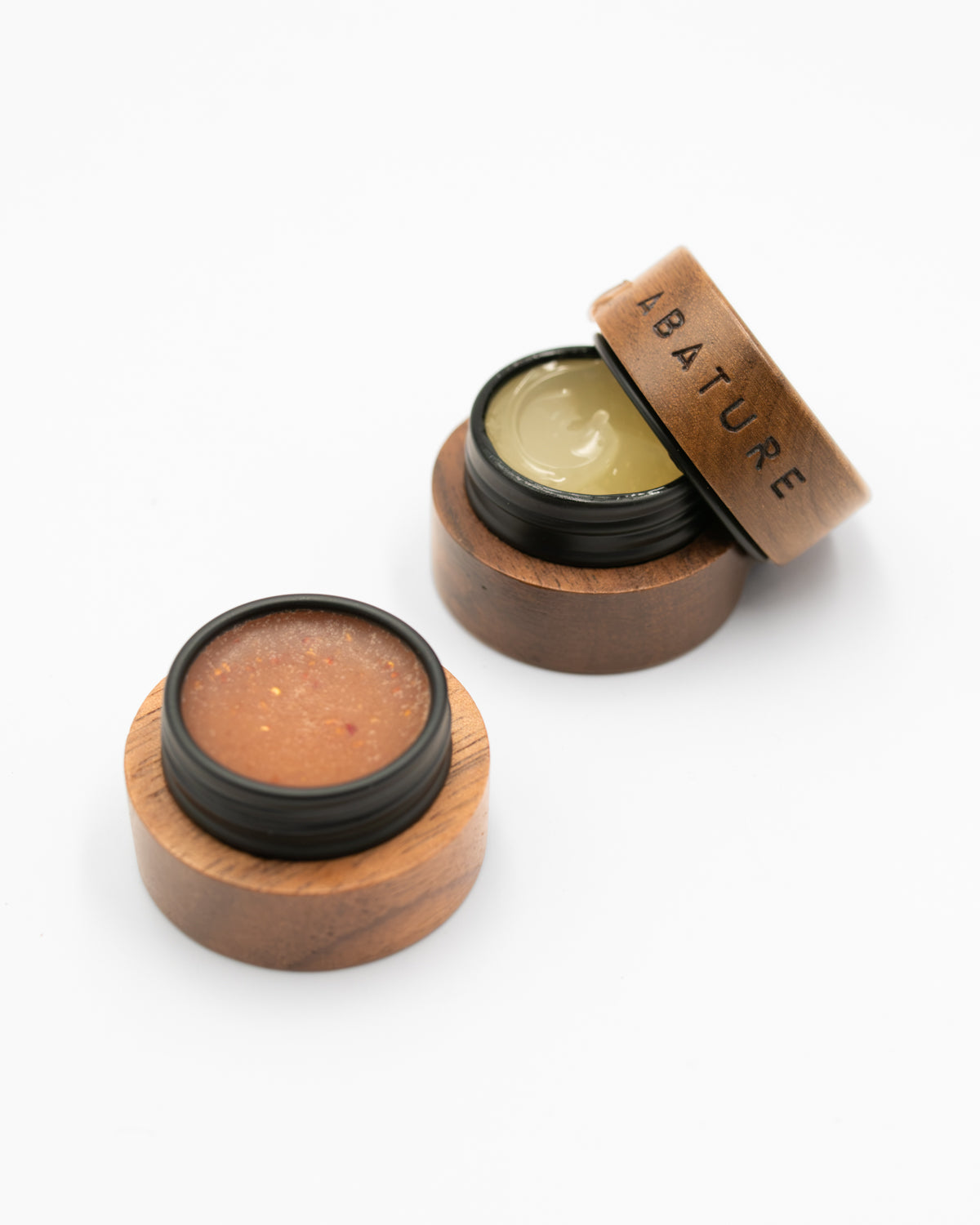 Open Abature lip scrub and serum pots with a wooden lid resting on top