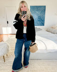 Selfie of a woman standing in a bedroom, wearing a black knit cardigan, graphic tee and jeans, holidng a beige fuzzy bag and wearing the East/West quartz statement cocktail ring in sterling silver.