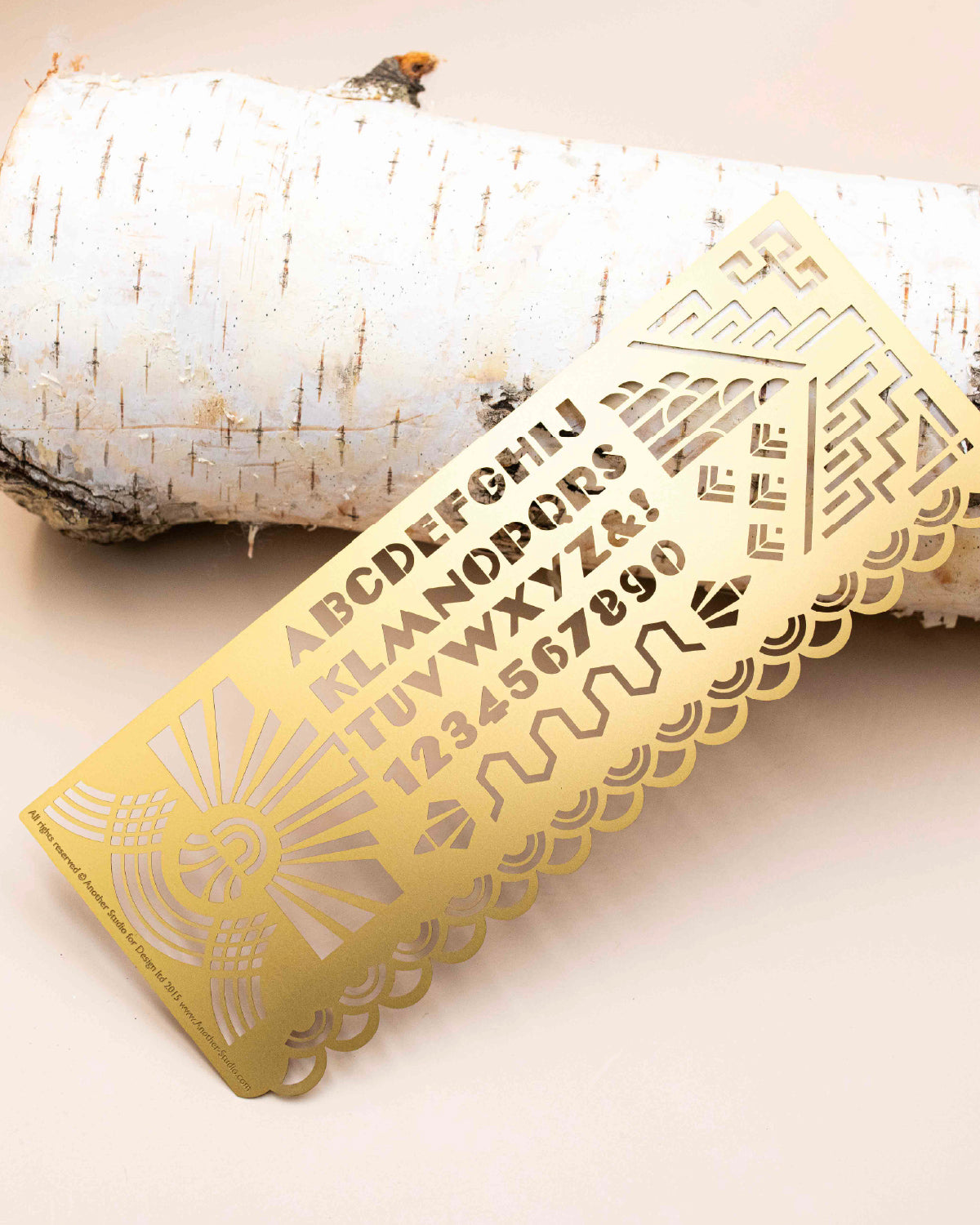 Another Studio brass art deco stencil with alphabet and sunburst cutouts on a birch log