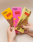 Hands holding Antidote dark chocolate bars in Mango Juniper, Rose Salt Lemon and Lemon Licorice