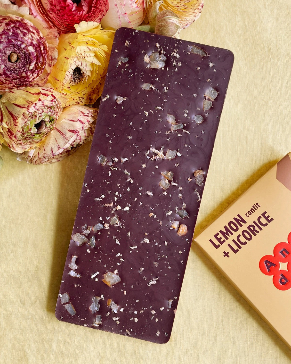 Antidote Lemon and Licorice dark chocolate bar studded with candied lemon, beside flowers