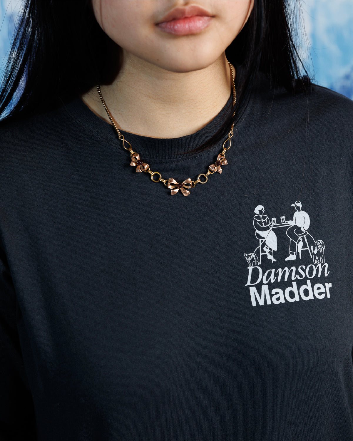 Woman wearing vintage,Van Dell two-toned rose and yellow gold-fill necklace with three sculptural bows on a 15&quot; chain over a black, graphic tee.