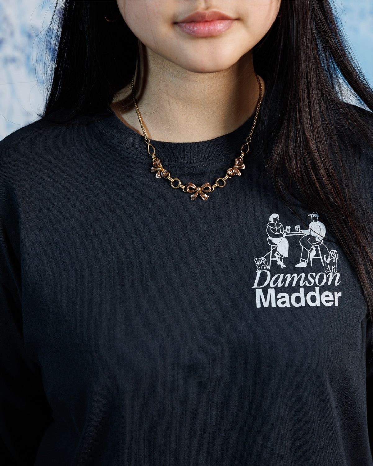 Woman wearing vintage,Van Dell two-toned rose and yellow gold-fill necklace with three sculptural bows on a 15&quot; chain over a black, graphic tee.