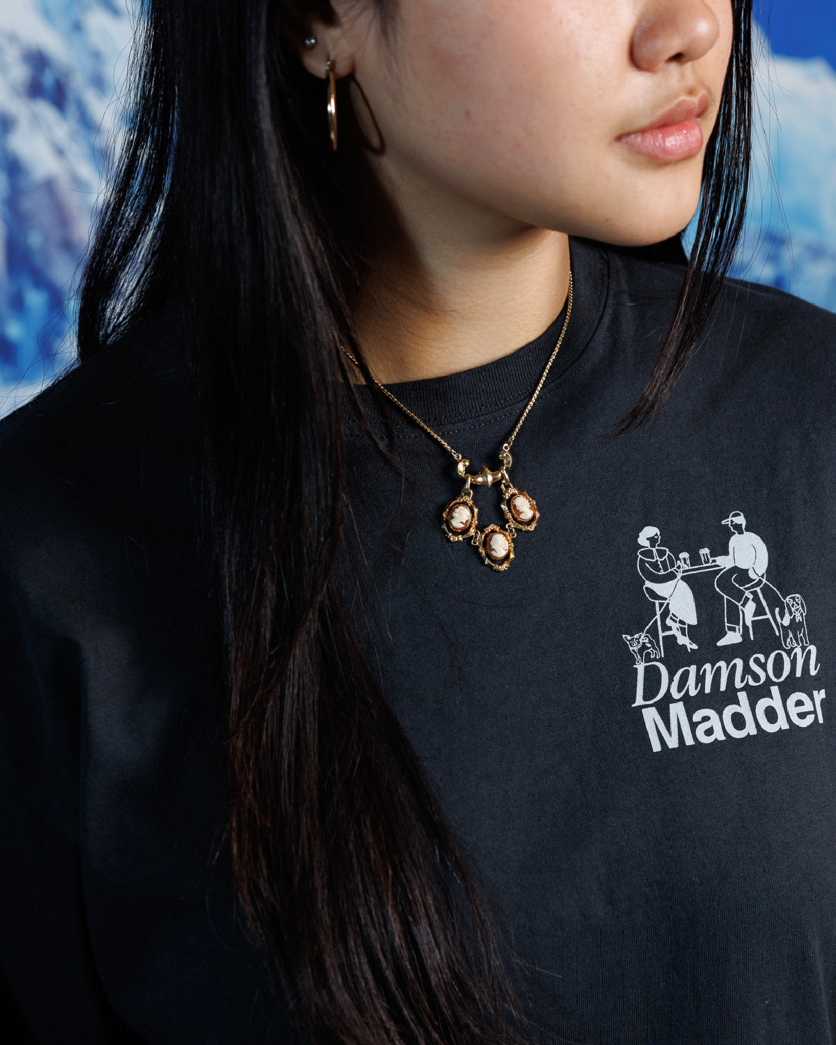 Woman wearing Victorian Revival gold-fill necklace with three carved shell cameos hanging from a gold-fill bar with delicate floral links in between, over a black, graphic tshirt.