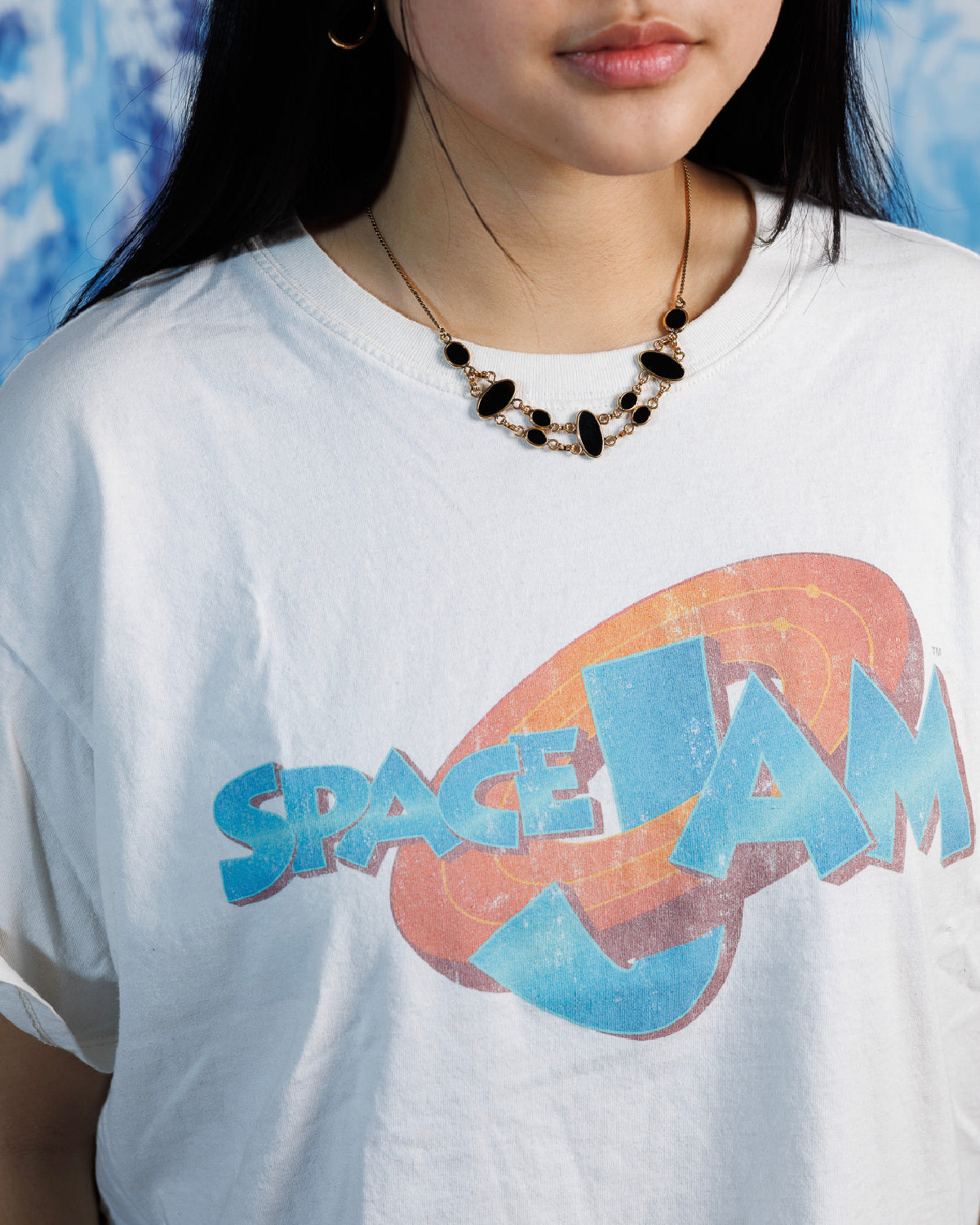 Close up of woman wearing gold-fill necklace featuring nine various sized, polished onyx stones connected via gold-fill links on a white graphic t-shirt