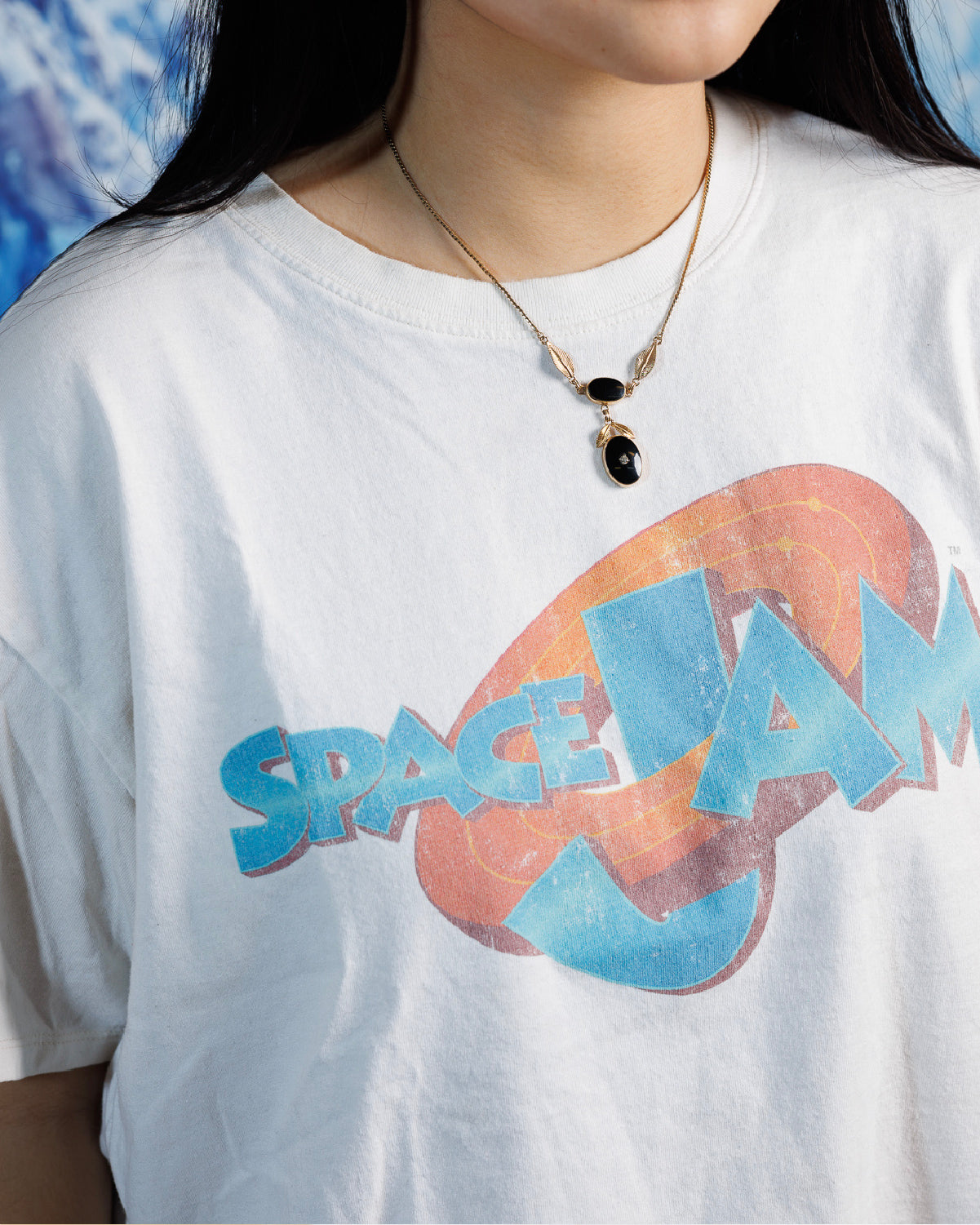 Close up of woman wearing gold-fill necklace with two onyx stones in a drop-style design with gold-fill leaf accents and a central rhinestone on a white graphic tshirt