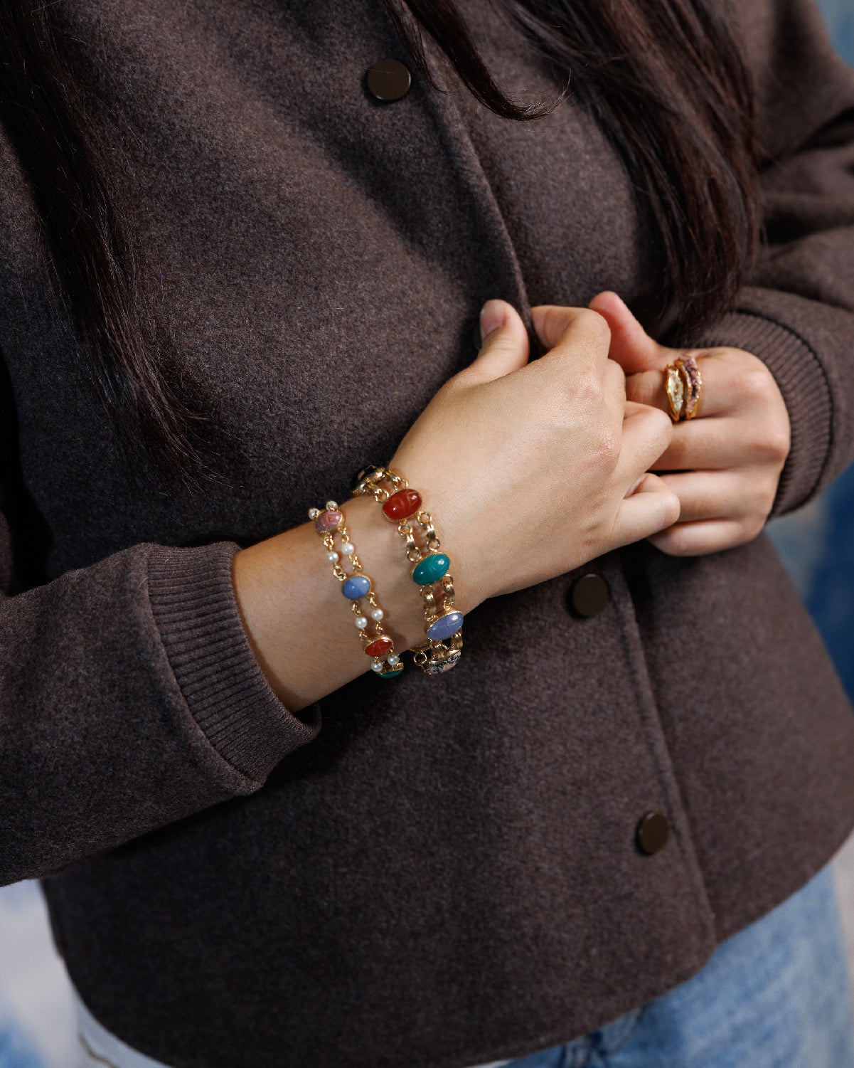 Close up of a person in brown sweater wearing two antique gold-filled scarab stone bracelets with double link settings.