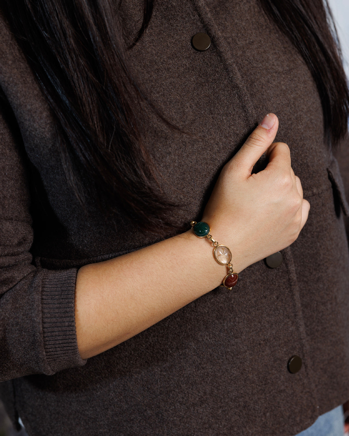 Close up of woman&#39;s arm in a brown sweater wearing an antique scarab bracelet featuring rare clear quartz, carnelian and green chalcedony.