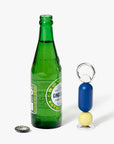 Blue, yellow bottle opener next to a green glass bottle. 