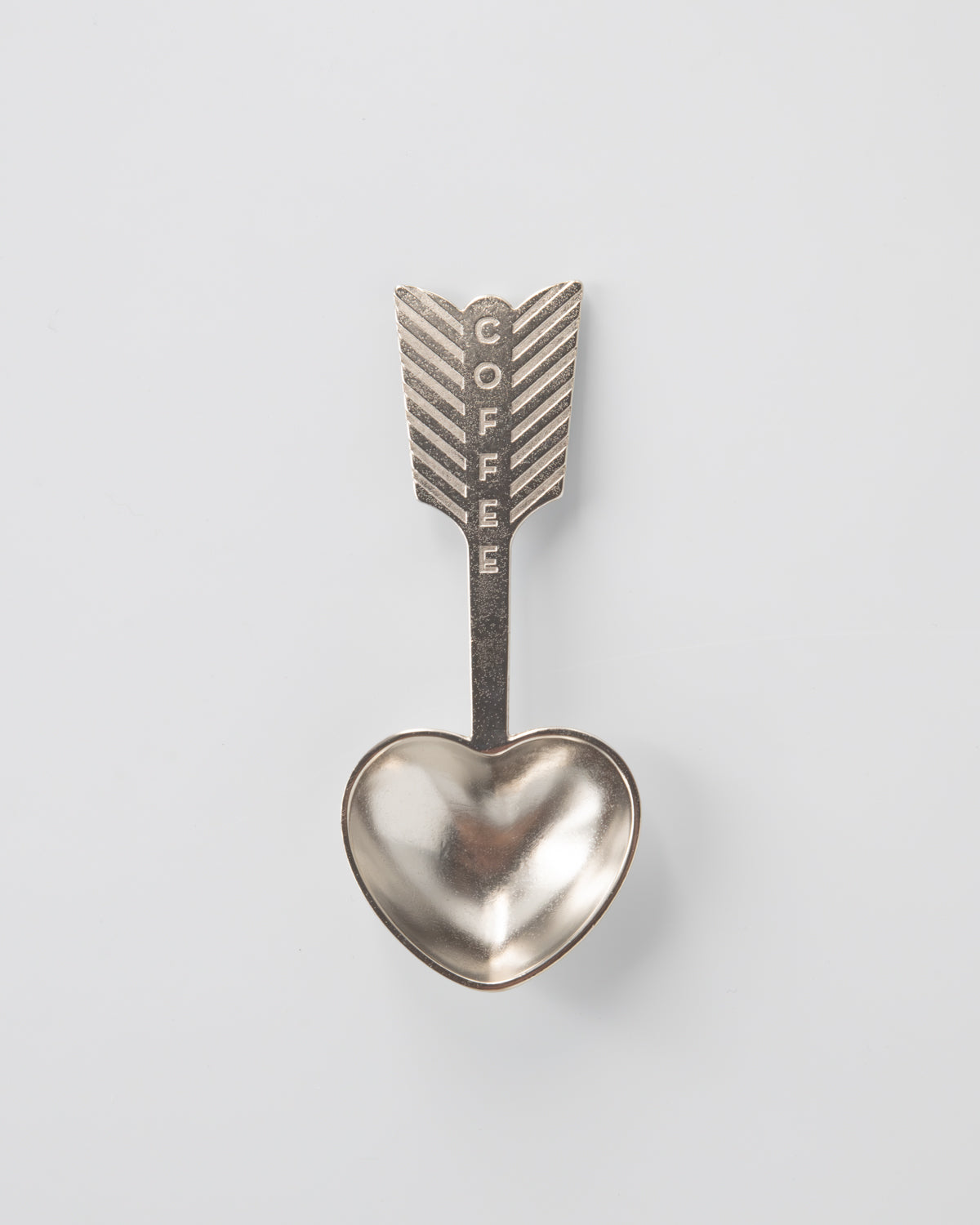 Metallic heart-shaped spoon with arrow design and 'COFFEE' text on a light gray background