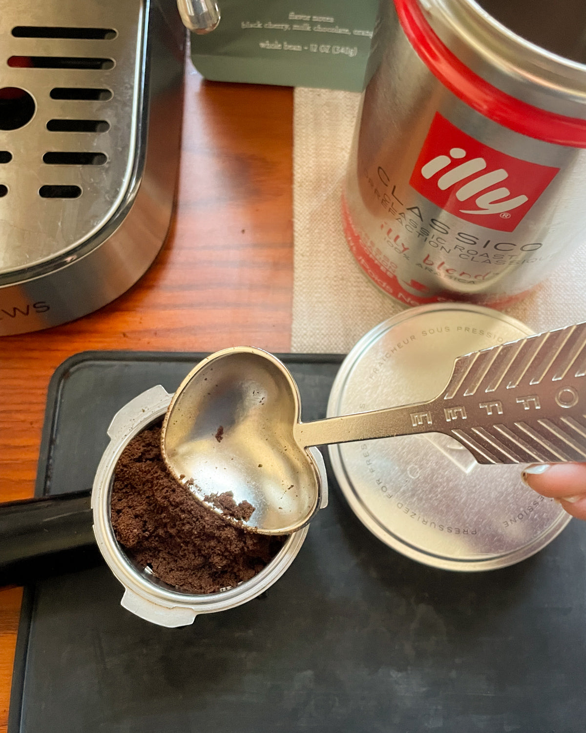Handmade heart-shaped metal coffee scoop measuring ground espresso beside an espresso machine