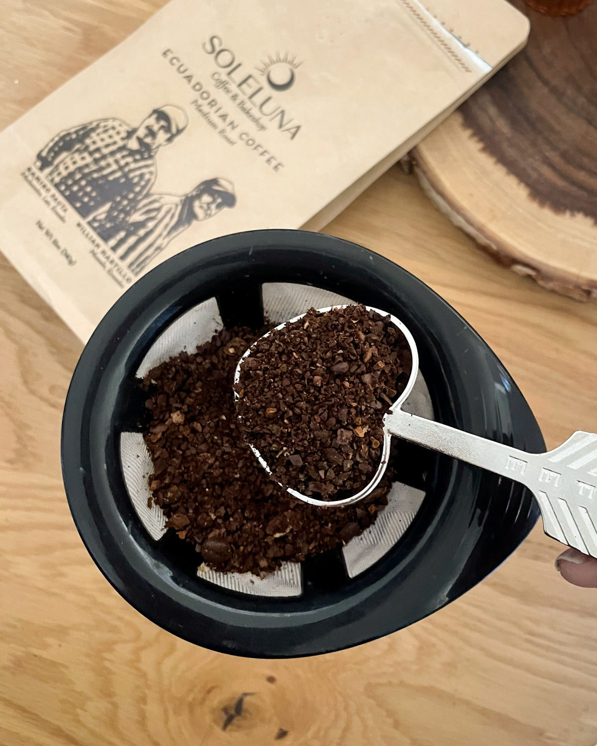 Heart-shaped handmade coffee scoop holding ground coffee over a pour-over coffee dripper.