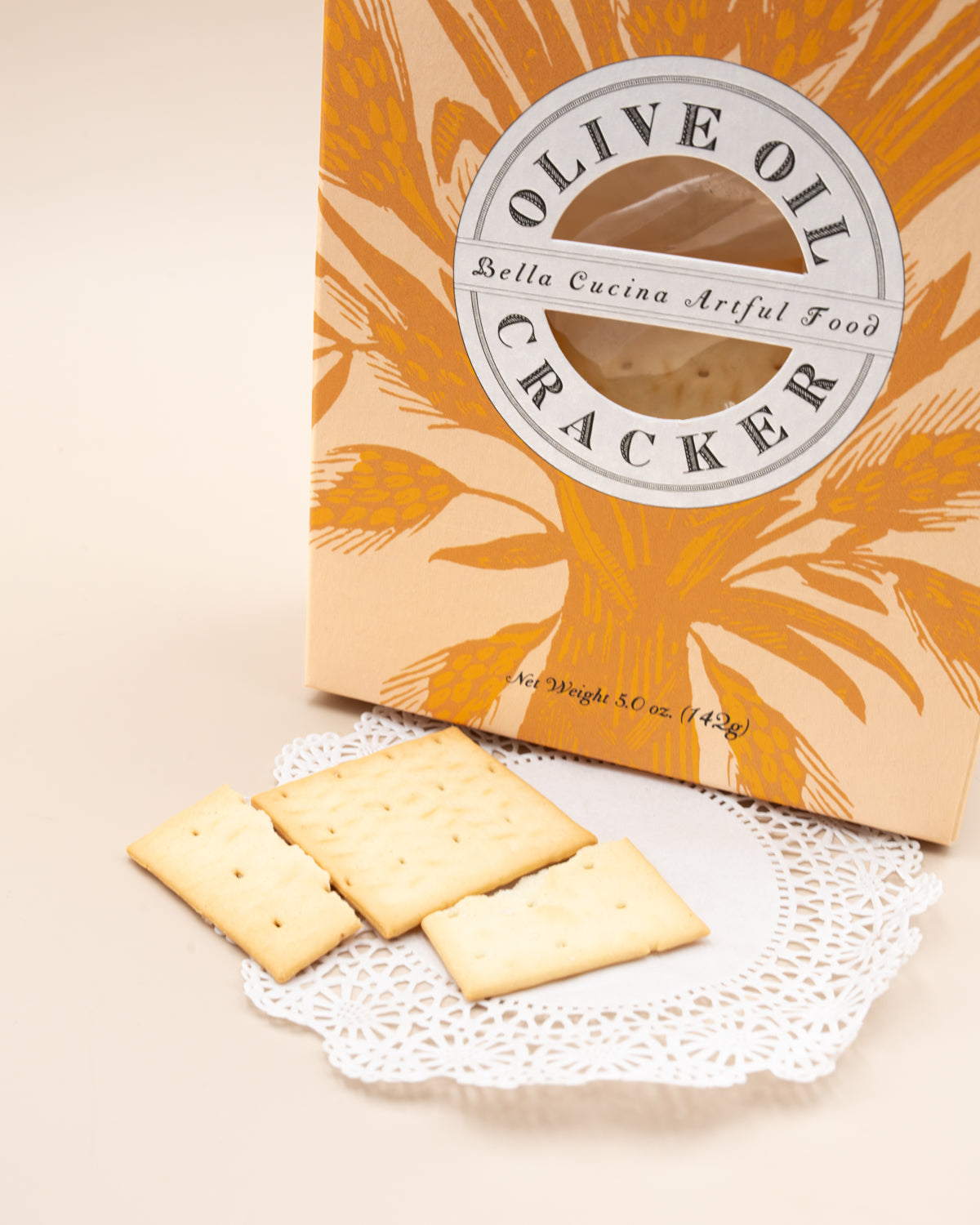 Bella Cucina Olive Oil Cracker box with square crackers on a lace doily