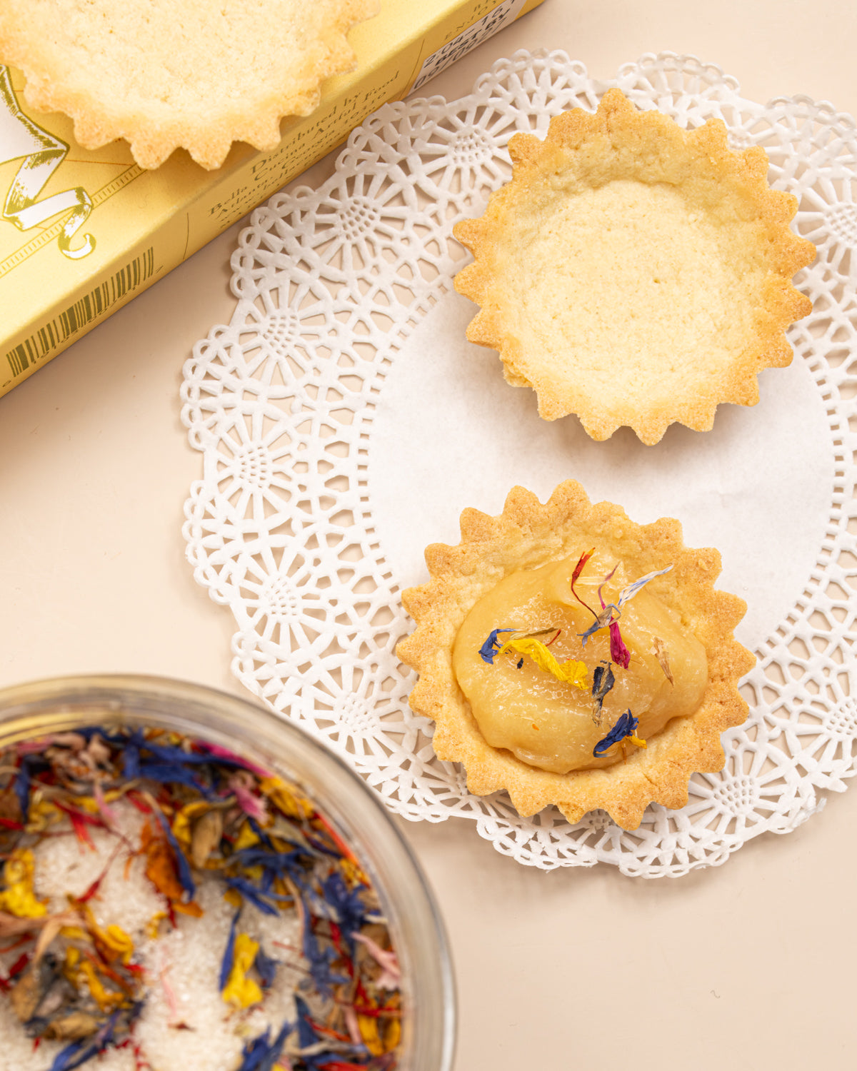 Mini tart shells topped with wildflower sugar beside a glass bowl of the sugar