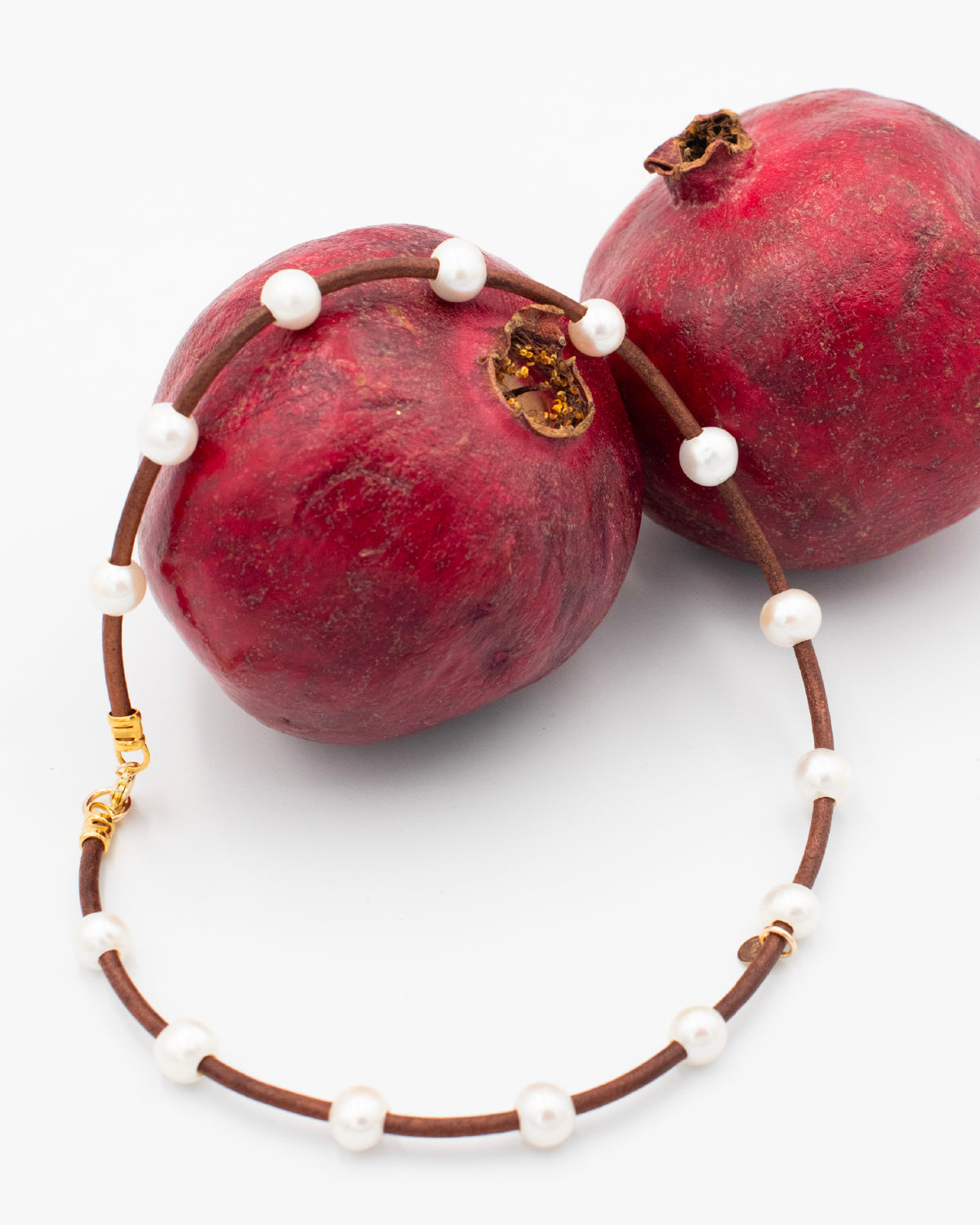 Necklace featuring hand strung pearls spaced out on a leather cord draped on a pomegranate